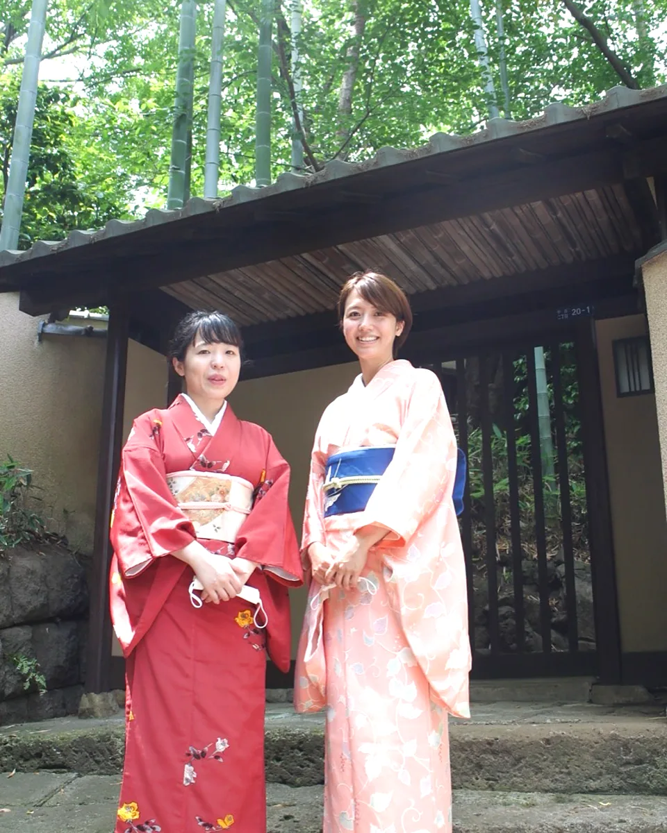 Two guests wearing kimono in front of a bamboo-lined gate